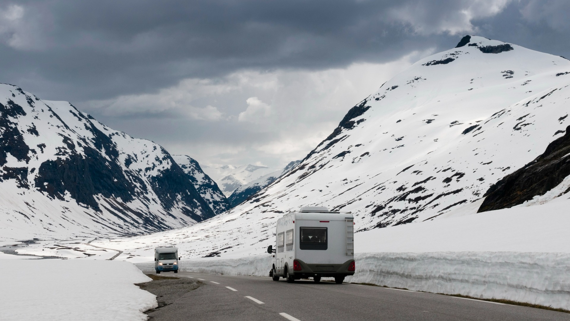 Vue arrière d'une roulotte sur la route entre deux montagnes enneigées.